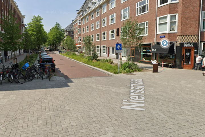 De Niersstraat 'after'. De straat is ‘rainproof’ gemaakt door een rij parkeerplaatsen te vervangen door groen. De wadi’s in de vorm van groene veldjes vangen het water goed op.